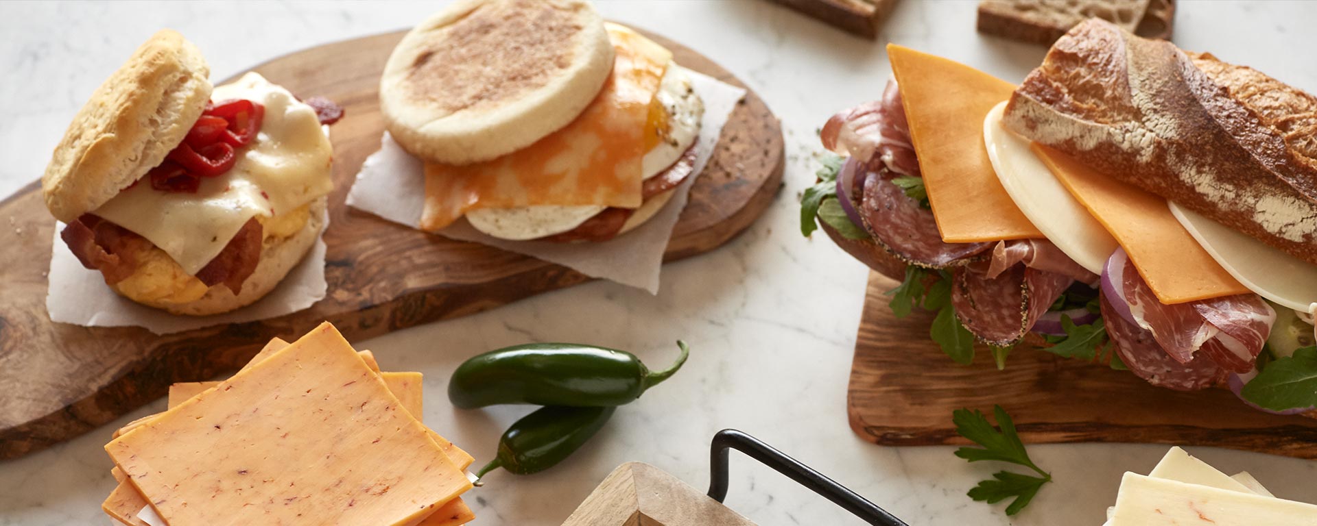 Breakfast sandwiches with cheese, and a sub sandwich plated nicely on a marble surface.